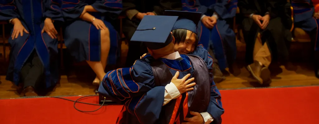 Graduate and advisor hugging at doctoral hooding ceremony